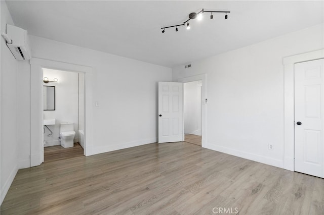 unfurnished bedroom with a closet, light hardwood / wood-style flooring, ensuite bath, and a wall mounted AC