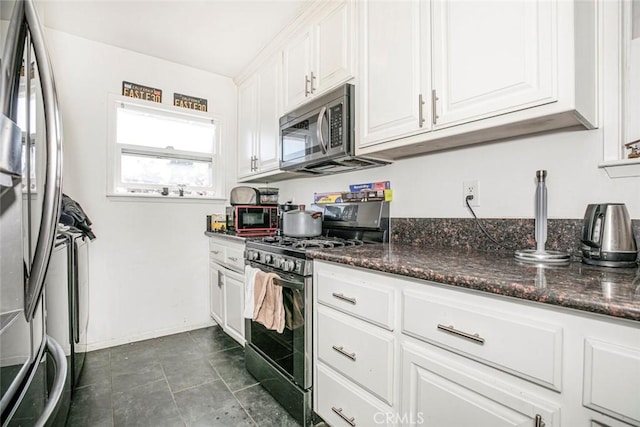 kitchen with white cabinets, dark tile patterned flooring, appliances with stainless steel finishes, and dark stone counters