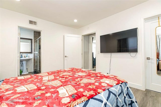 bedroom with ensuite bathroom, hardwood / wood-style floors, and sink