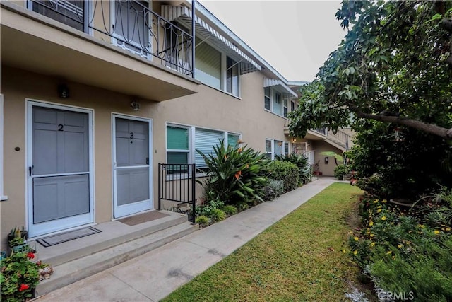 view of exterior entry featuring a lawn and stucco siding