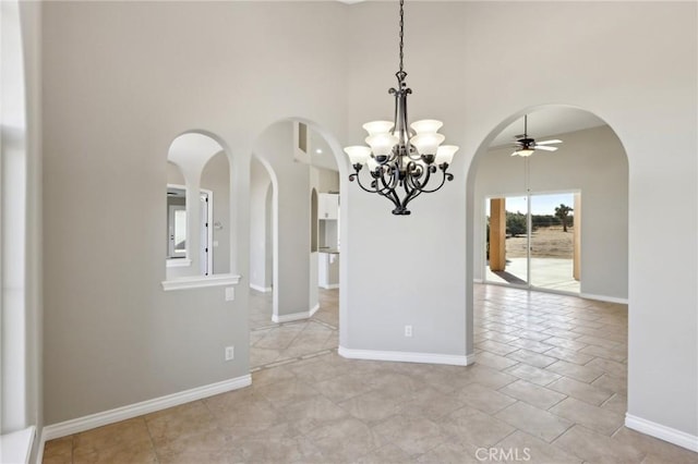 unfurnished dining area featuring ceiling fan with notable chandelier and a high ceiling