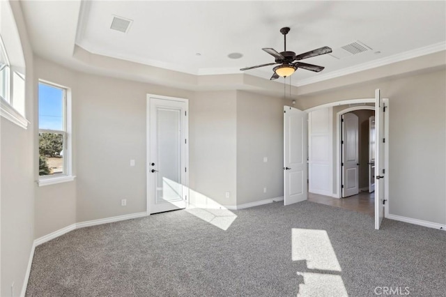 unfurnished bedroom featuring ceiling fan, dark carpet, a tray ceiling, and ornamental molding