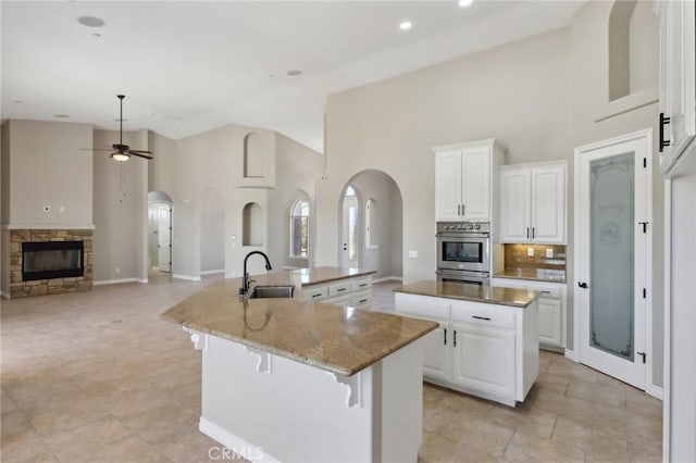 kitchen with ceiling fan, sink, white cabinets, and an island with sink