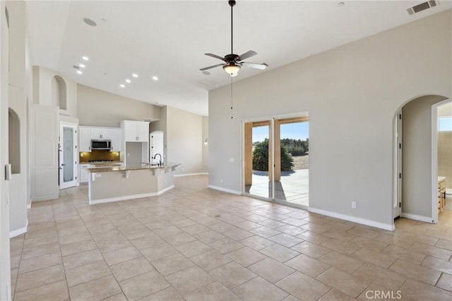 unfurnished living room featuring ceiling fan, light tile patterned floors, sink, and high vaulted ceiling