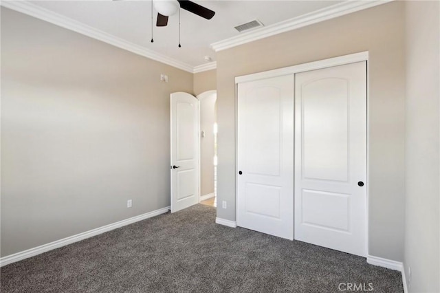 unfurnished bedroom featuring ceiling fan, a closet, crown molding, and dark colored carpet