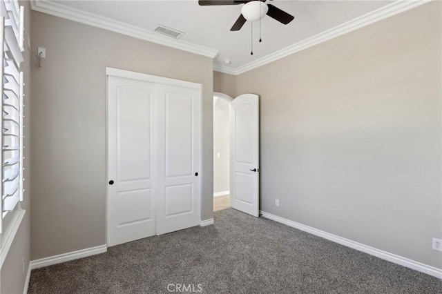 unfurnished bedroom featuring ceiling fan, ornamental molding, a closet, and dark carpet