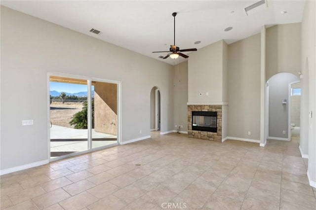 unfurnished living room featuring ceiling fan, light tile patterned floors, a high ceiling, and a stone fireplace