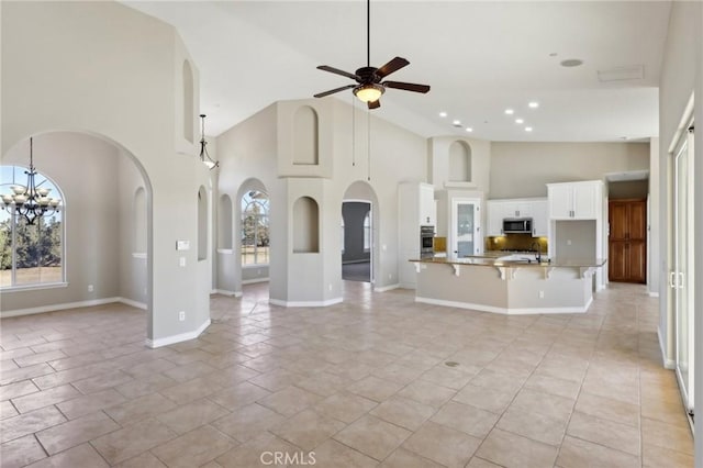 unfurnished living room with ceiling fan with notable chandelier, sink, a wealth of natural light, and a towering ceiling