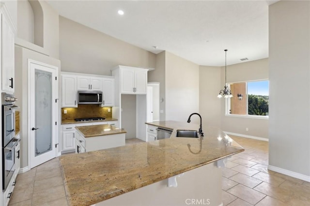 kitchen featuring an island with sink, appliances with stainless steel finishes, light stone countertops, white cabinets, and sink