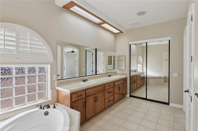 bathroom with ceiling fan, tile patterned flooring, tiled tub, and vanity