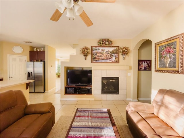 living area with visible vents, ceiling fan, a tiled fireplace, and light tile patterned floors