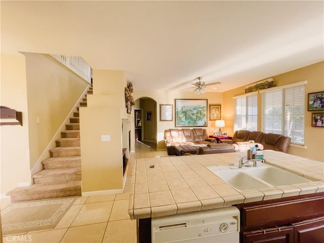 kitchen with light tile patterned floors, arched walkways, dishwasher, tile countertops, and a sink