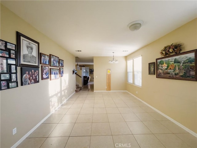 unfurnished room featuring light tile patterned floors, baseboards, and an inviting chandelier