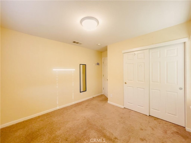 unfurnished bedroom featuring baseboards, visible vents, a closet, and light colored carpet