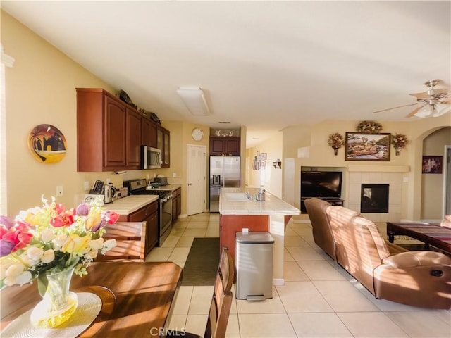 kitchen with a fireplace, light tile patterned floors, stainless steel appliances, tile counters, and open floor plan