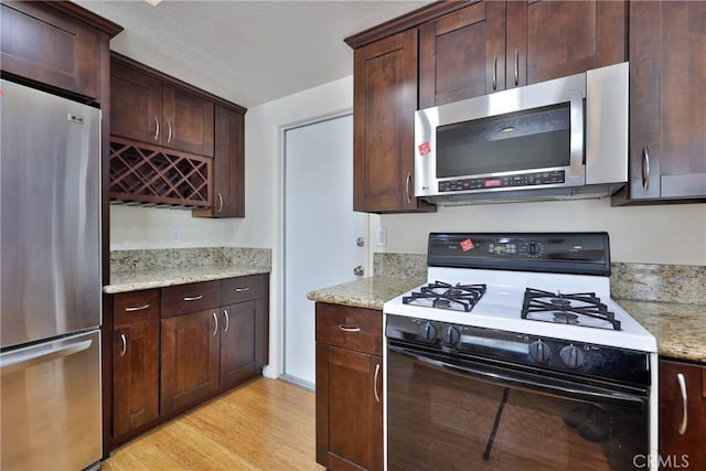 kitchen featuring dark brown cabinetry, light stone countertops, stainless steel appliances, and light hardwood / wood-style flooring