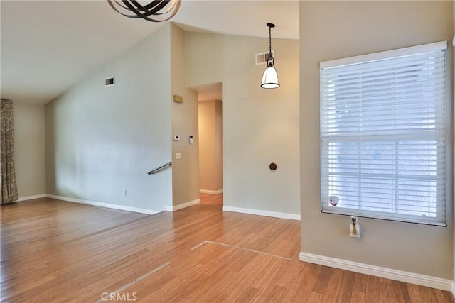 unfurnished room with high vaulted ceiling, an inviting chandelier, and hardwood / wood-style floors