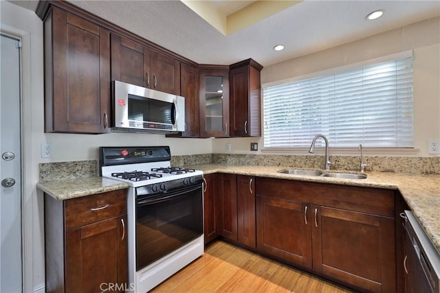 kitchen featuring sink, dark brown cabinetry, light wood-type flooring, appliances with stainless steel finishes, and light stone counters