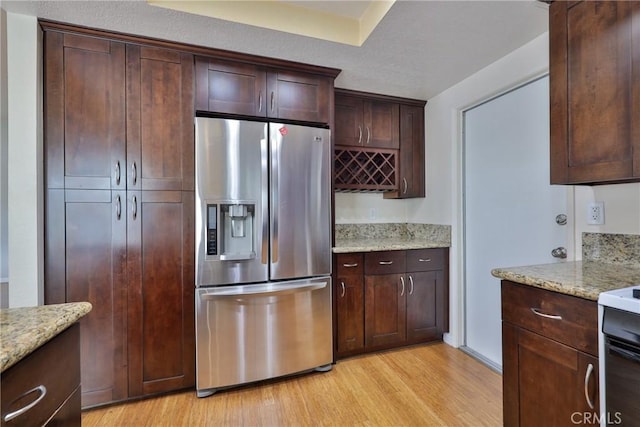 kitchen featuring light hardwood / wood-style floors, light stone countertops, dark brown cabinetry, and stainless steel fridge with ice dispenser