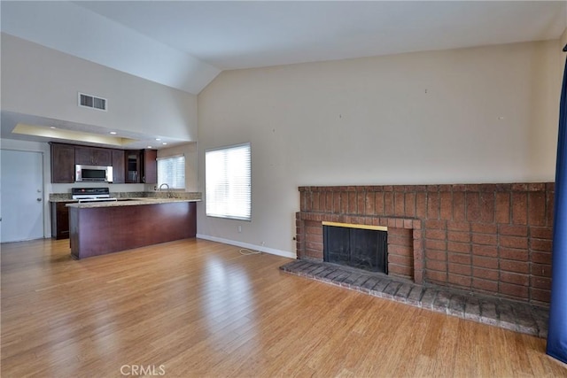 unfurnished living room featuring vaulted ceiling, a brick fireplace, and light hardwood / wood-style flooring