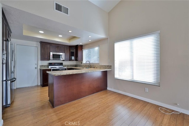 kitchen with kitchen peninsula, sink, dark brown cabinetry, light wood-type flooring, and appliances with stainless steel finishes