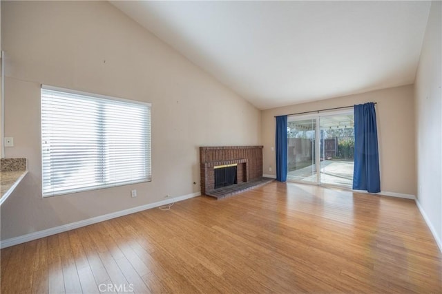 unfurnished living room featuring high vaulted ceiling, plenty of natural light, light hardwood / wood-style floors, and a brick fireplace