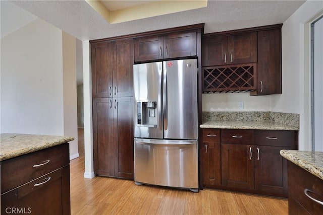 kitchen featuring stainless steel fridge with ice dispenser, light hardwood / wood-style floors, dark brown cabinetry, and light stone countertops