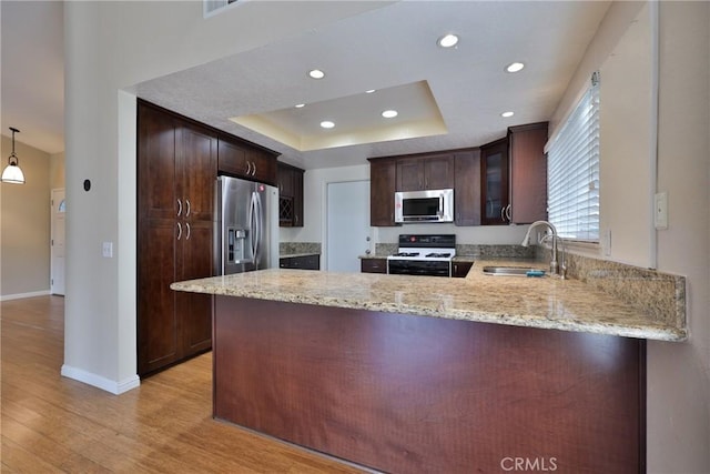 kitchen with kitchen peninsula, a raised ceiling, stainless steel appliances, and hanging light fixtures