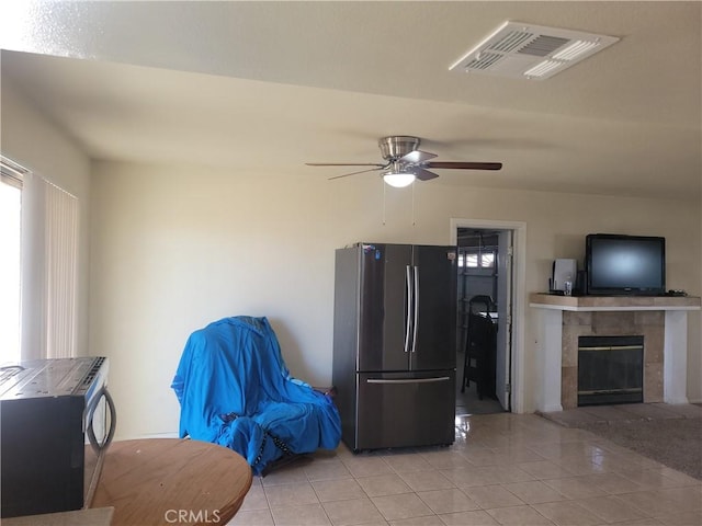 interior space featuring ceiling fan, a tiled fireplace, and light tile patterned flooring