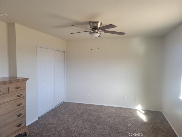 unfurnished bedroom with baseboards, dark colored carpet, a closet, and ceiling fan