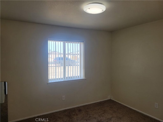 spare room with baseboards and dark colored carpet