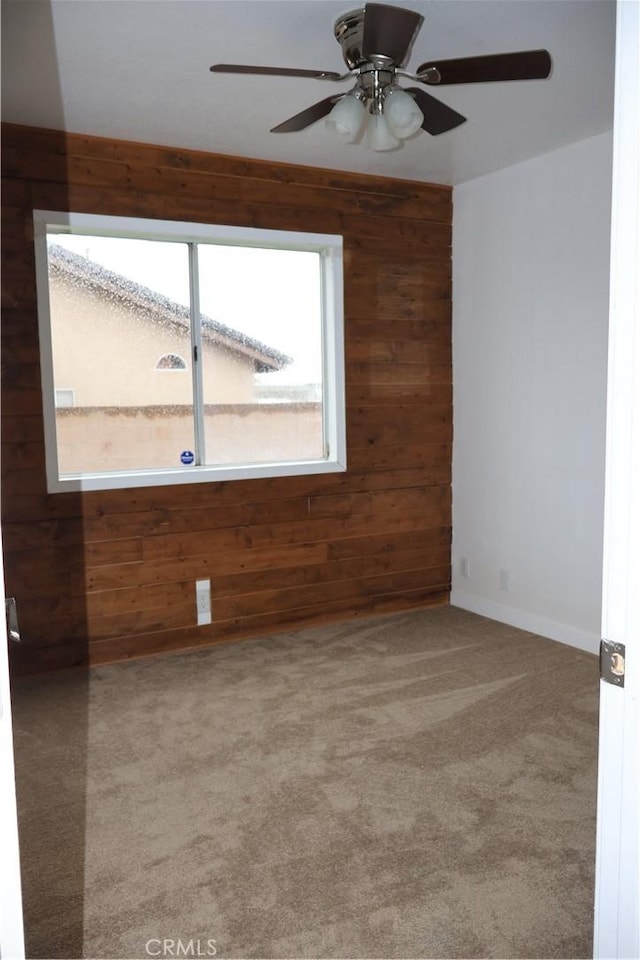 carpeted spare room featuring wooden walls and ceiling fan