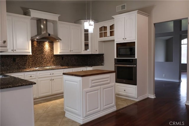 kitchen featuring pendant lighting, wall chimney range hood, appliances with stainless steel finishes, a center island, and white cabinets