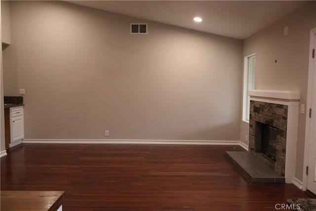 unfurnished living room featuring vaulted ceiling, a stone fireplace, and dark hardwood / wood-style flooring