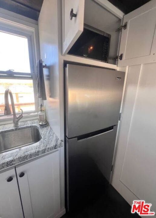 kitchen with white cabinets, sink, light stone countertops, and stainless steel refrigerator