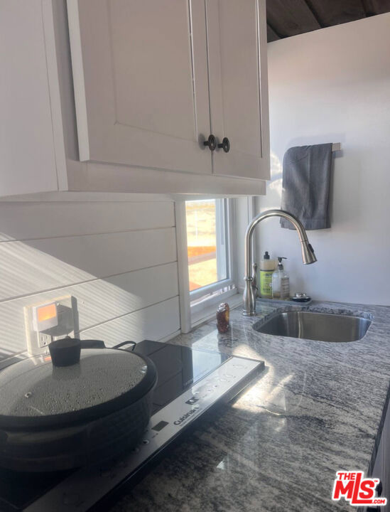 interior details featuring white cabinetry, dark stone counters, and sink