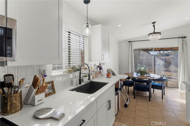 kitchen featuring light stone countertops, white cabinetry, hanging light fixtures, and sink