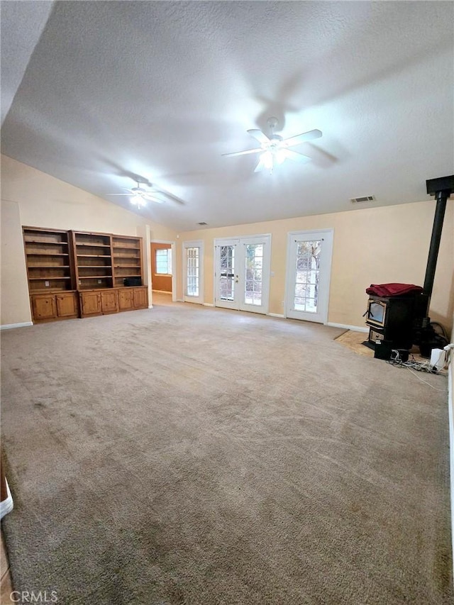 unfurnished living room with a textured ceiling, carpet, lofted ceiling, and a wood stove