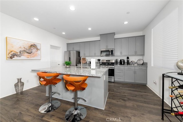 kitchen with appliances with stainless steel finishes, an island with sink, a breakfast bar, and light stone countertops