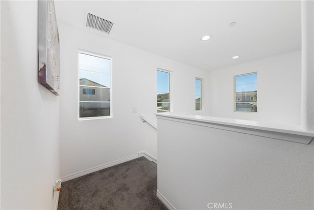 hall featuring dark colored carpet and a wealth of natural light