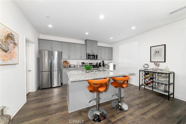 kitchen with a kitchen bar, appliances with stainless steel finishes, a kitchen island with sink, dark hardwood / wood-style flooring, and light stone counters