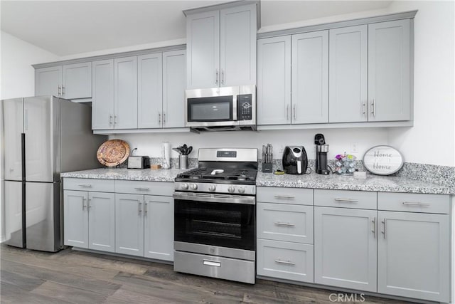 kitchen with dark wood-type flooring, gray cabinetry, appliances with stainless steel finishes, and light stone counters