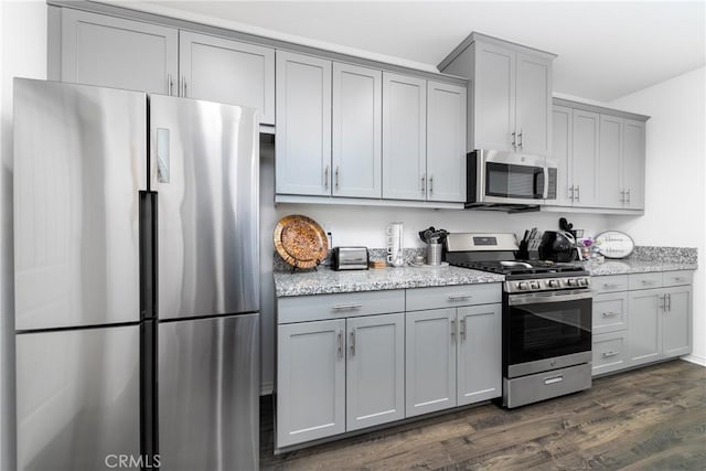 kitchen with dark wood-type flooring, appliances with stainless steel finishes, light stone counters, and gray cabinets