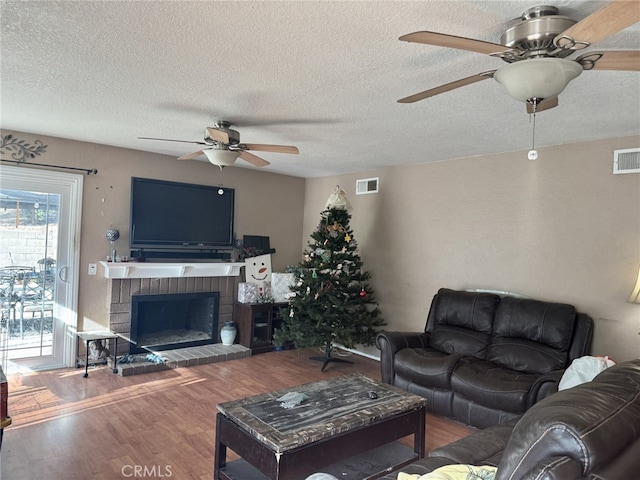 living room with ceiling fan, wood-type flooring, a brick fireplace, and a textured ceiling