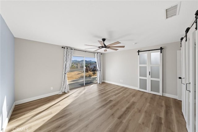 unfurnished room featuring a barn door, visible vents, ceiling fan, and wood finished floors