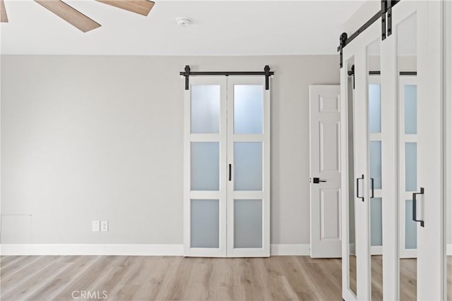 unfurnished bedroom with light wood-style floors, a ceiling fan, baseboards, and a barn door