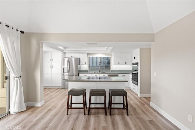 kitchen with a breakfast bar area, appliances with stainless steel finishes, white cabinets, a sink, and light wood-type flooring