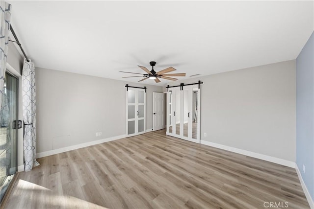 interior space featuring light wood-style floors, ceiling fan, baseboards, and a barn door