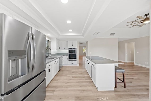 kitchen with stainless steel appliances, a tray ceiling, light wood-type flooring, and a kitchen breakfast bar