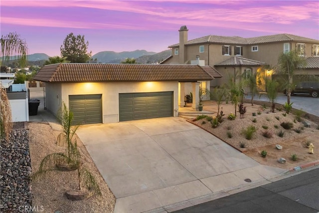 mediterranean / spanish-style home with a tile roof, driveway, an attached garage, and stucco siding